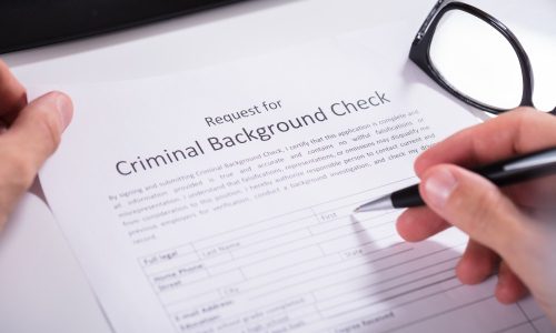 Close-up Of Person Hand Filling Criminal Background Check Application Form