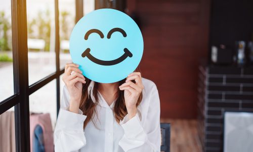 Woman holding happy face cut out up to face, work-life balance, work-life wellbeing