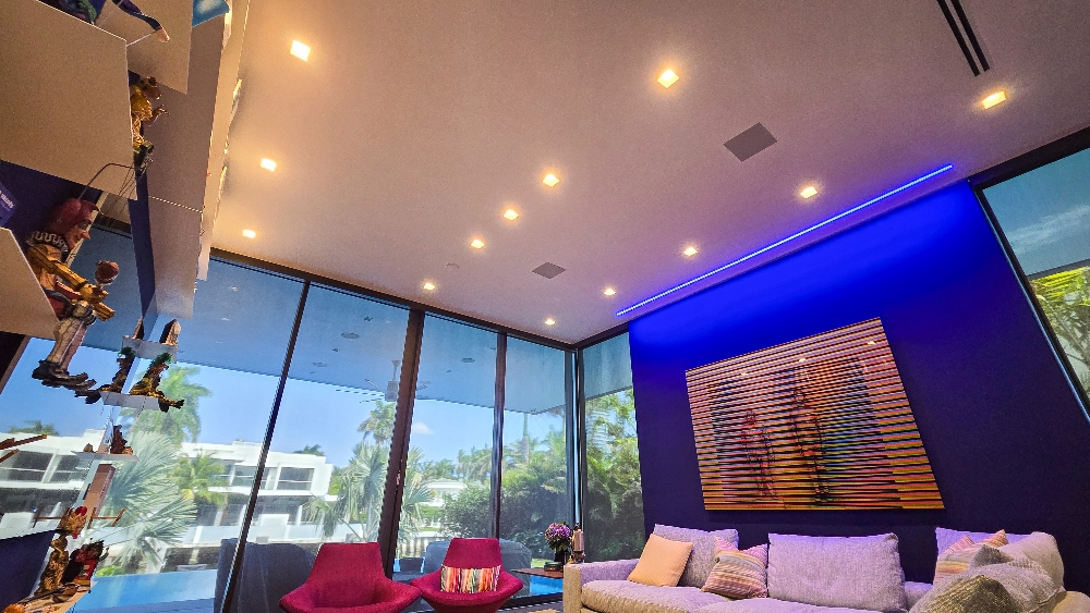 Living room entertainment area with colorful blue walls and custom artwork under warm downlighting.