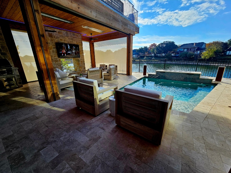 Exterior stone patio area with plush seating arrangement near in-ground pool overlooking lake in background McKinney Texas